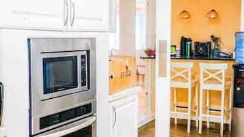 A kitchen with white cabinets, a microwave, and an oven. There is a dining area with a table and chairs.