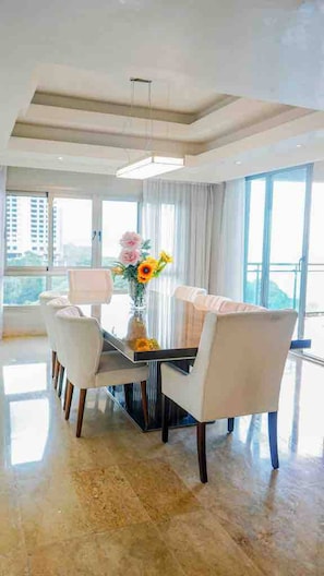 Uma área de jantar moderna com mesa de vidro, cadeiras brancas e um vaso de flores.