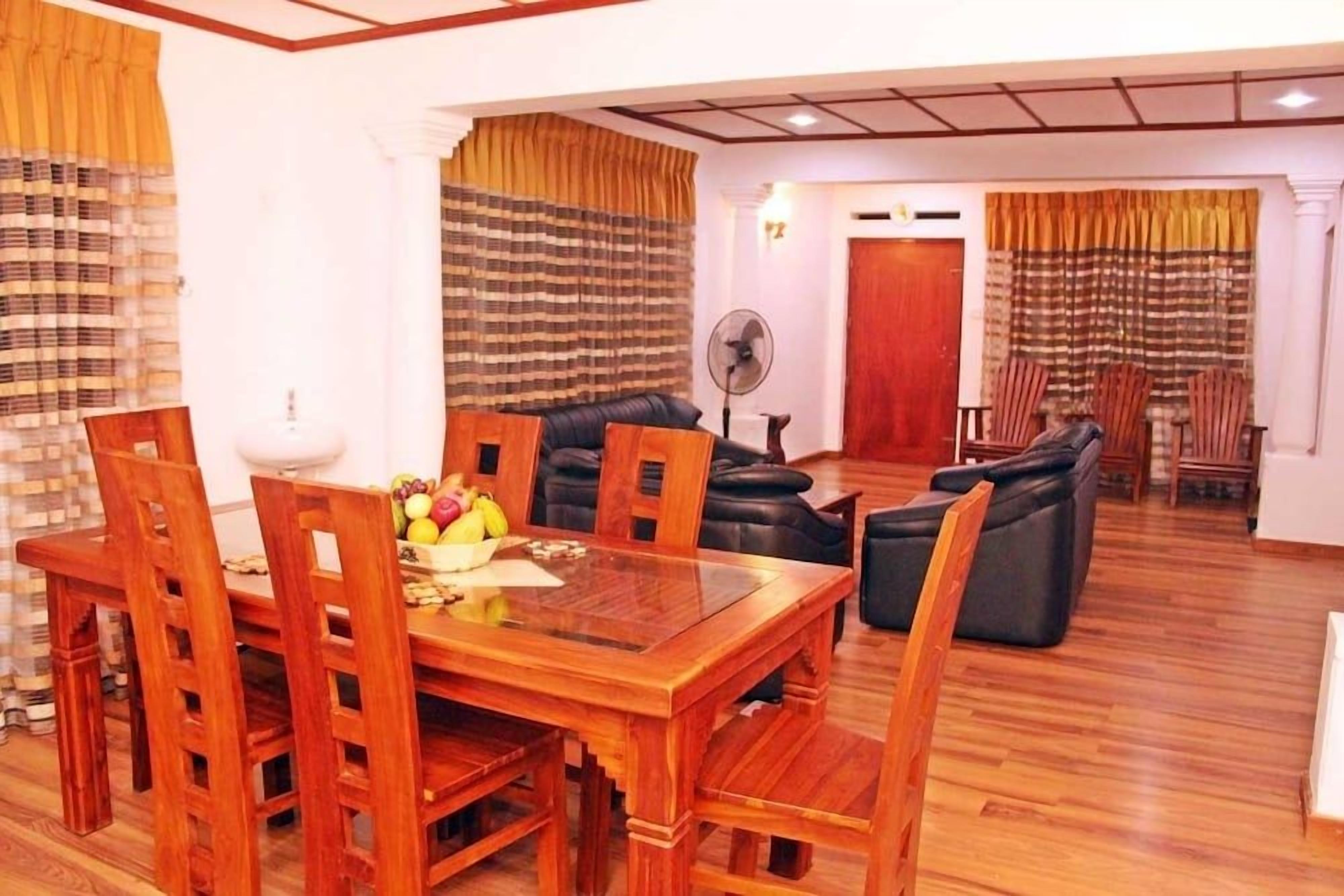 A dining area with a wooden table and chairs, a fan, and a seating area with sofas and curtains.