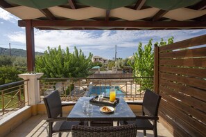 Un espacio de estar al aire libre techado con vista a la piscina, muebles de mimbre y una mesa con bebidas y aperitivos.