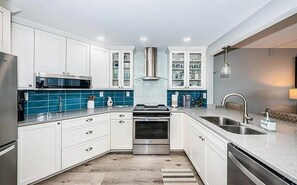 A modern kitchen with white cabinets, a stainless steel range hood, and a double sink. -  NEW LISTING Water View Condo (St. Petersburg)