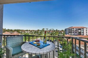 A balcony with a wicker chair and a round table, a bottle of wine, and a bowl of fruit. -  NEW LISTING Water View Condo (St. Petersburg)