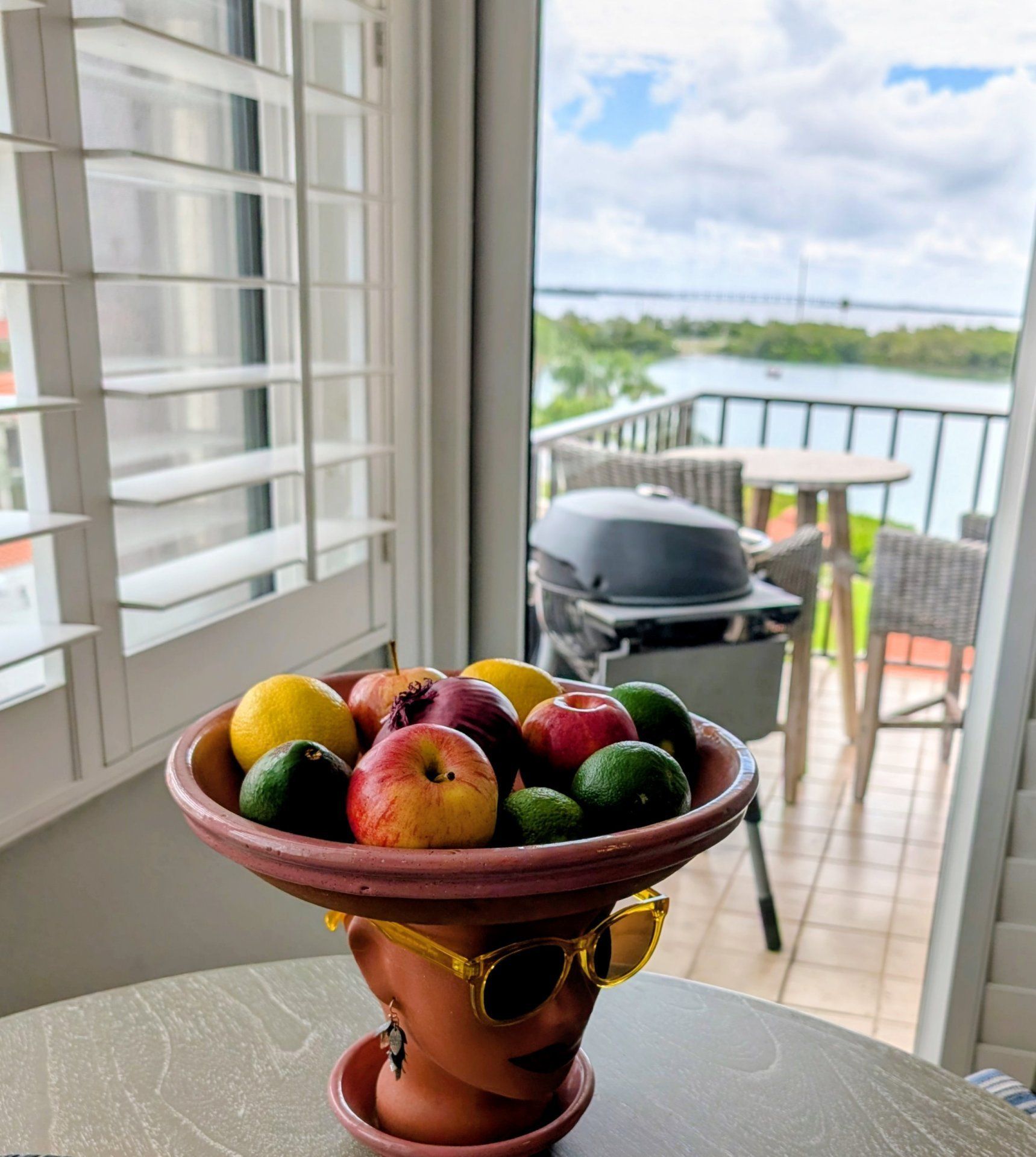 Un balcón con una mesa que sostiene un bol de fruta y una parrilla.