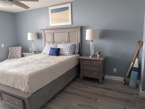Ein Schlafzimmer mit einem Bett, Nachttischen, einer Kommode, einem Deckenventilator und einem gerahmten Bild an der Wand.