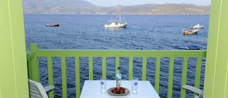 A balcony with a table and chairs, overlooking a calm sea with several boats.
