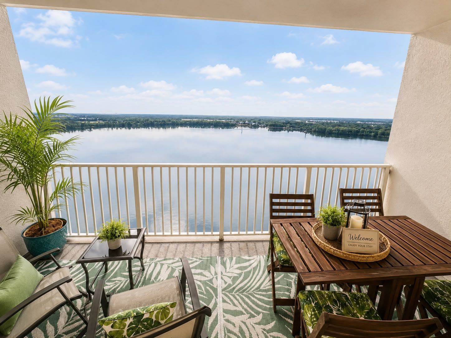 A balcony with a view of a lake, a wooden table with a sign, and seating arrangements.