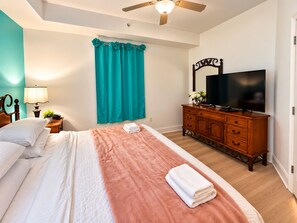 Una habitación de hotel con cama, televisor, cómoda y ventilador de techo.