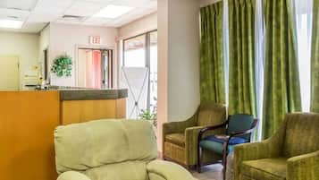 A hotel lobby with a reception desk, a seating area with armchairs, and a large window with curtains.