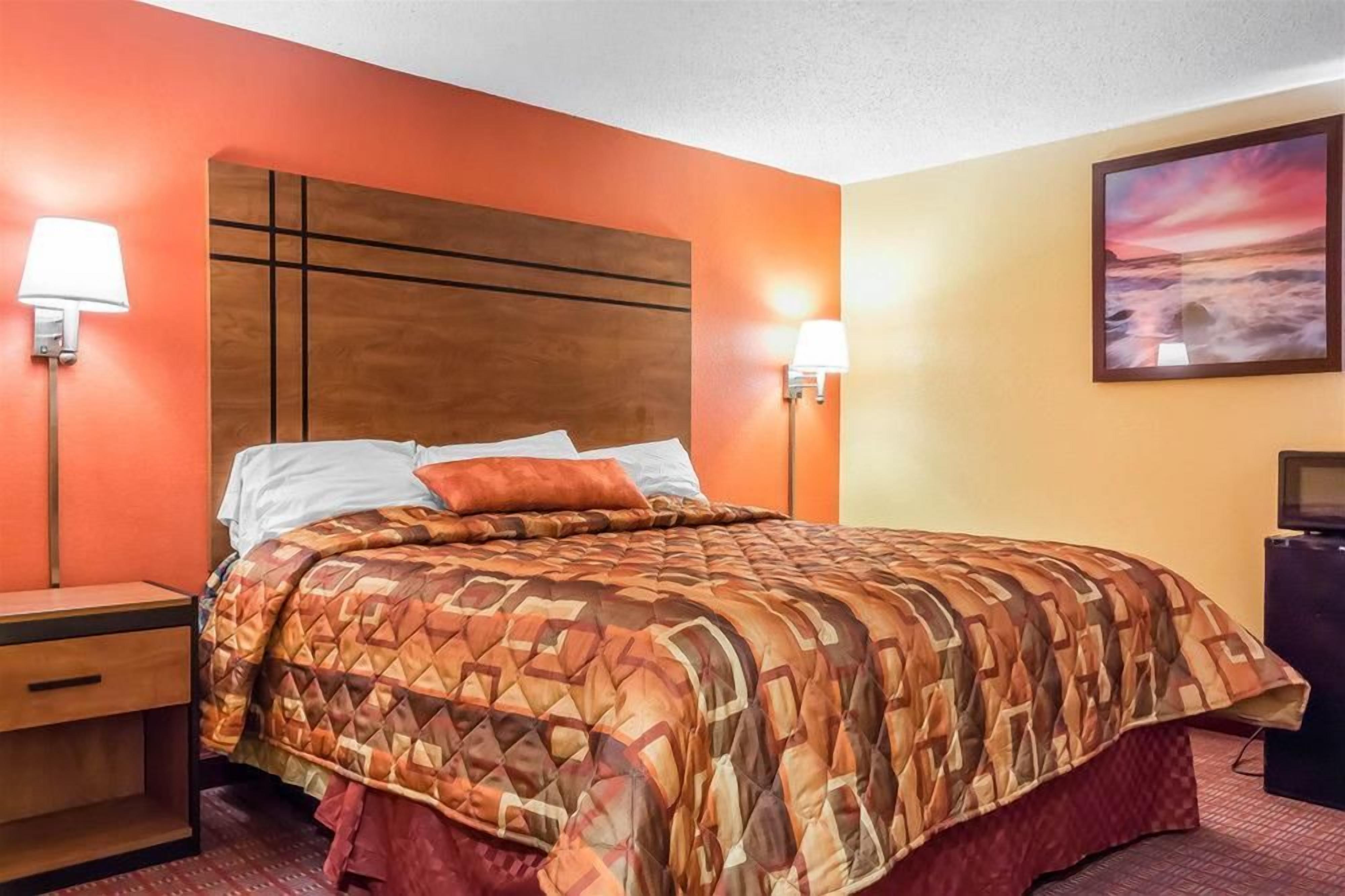 A hotel room with a bed, two bedside lamps, a nightstand, a TV, and a painting on the wall.