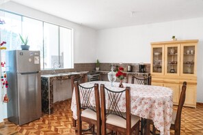 Eine Küche mit Kühlschrank, Esstisch mit Stühlen, Schrank und Fenster.