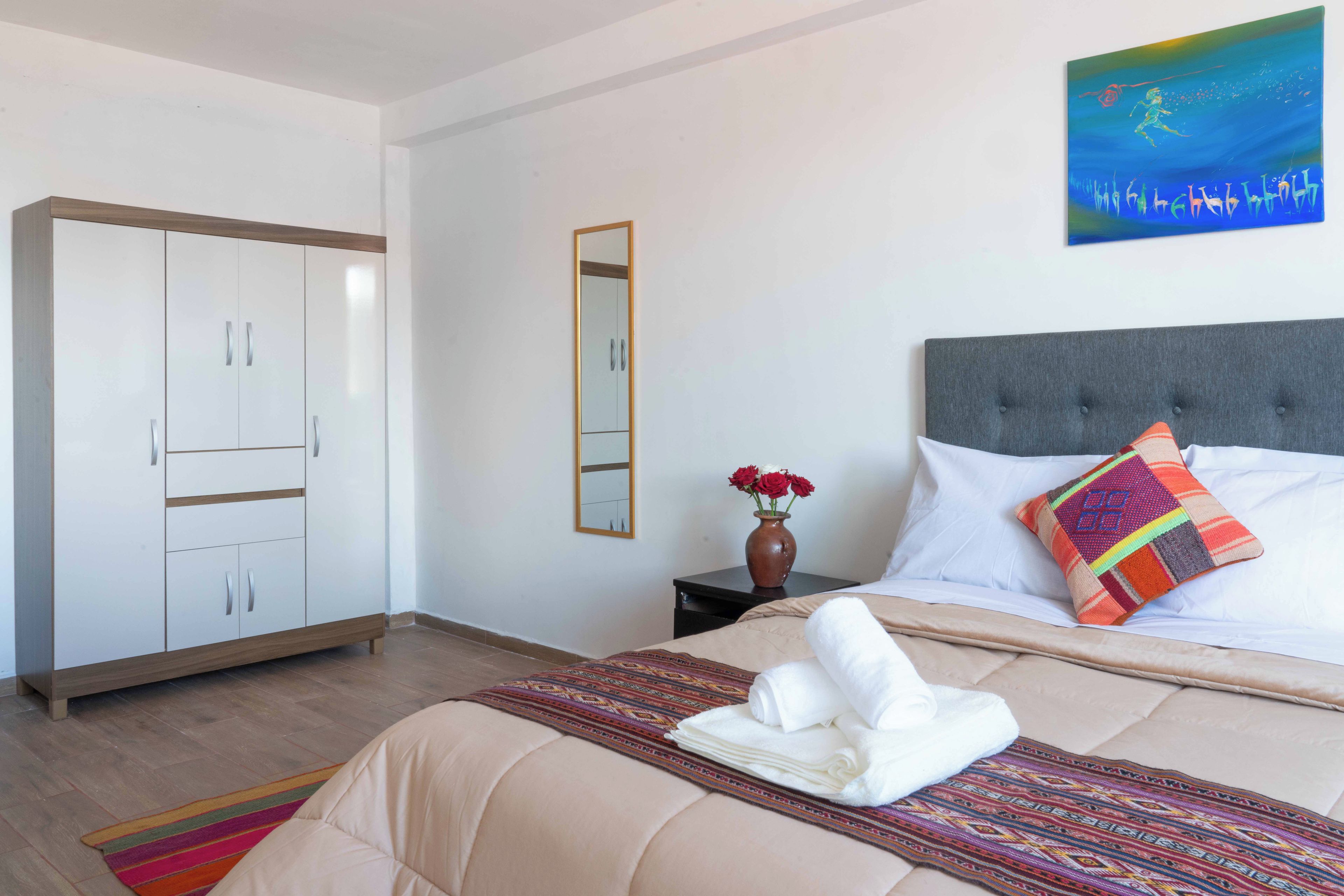 Una habitació d'hotel amb un llit, un armari, un mirall, un vas amb flors i un quadre a la paret.
