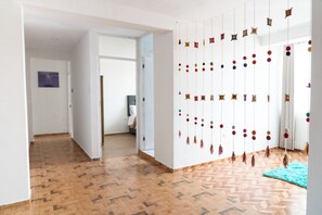 Ein Flur mit gemustertem Holzboden, einer weißen Wand mit einem gerahmten Bild und einer Wanddekoration mit bunten Pompons.
