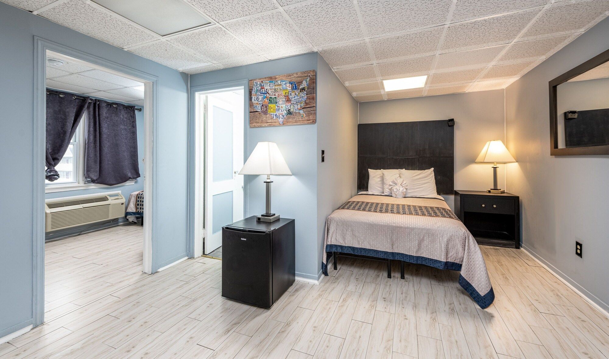 A hotel room with a bed, two bedside lamps, a wall-mounted map, a heater, and a window with curtains.