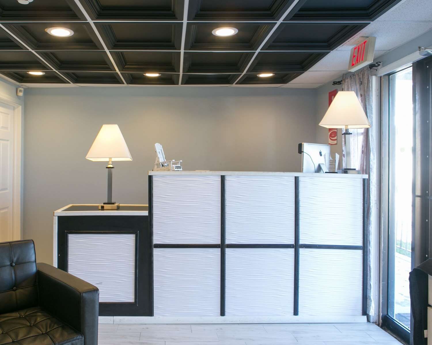 A reception area with a desk, two lamps, a black leather chair, and a view of the outside through a glass door.