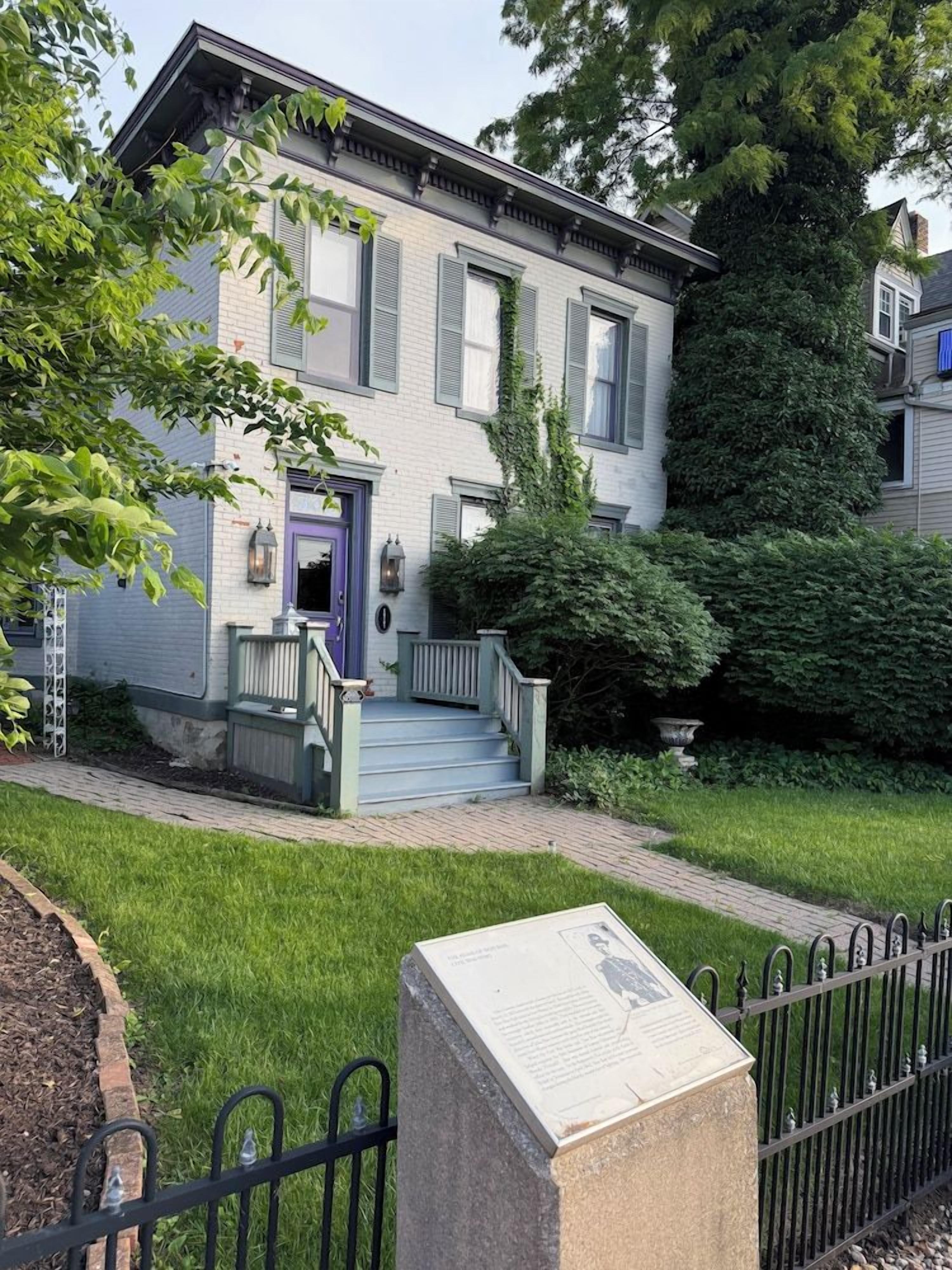 A two-story house with a front porch, a purple door, and a stone plaque.