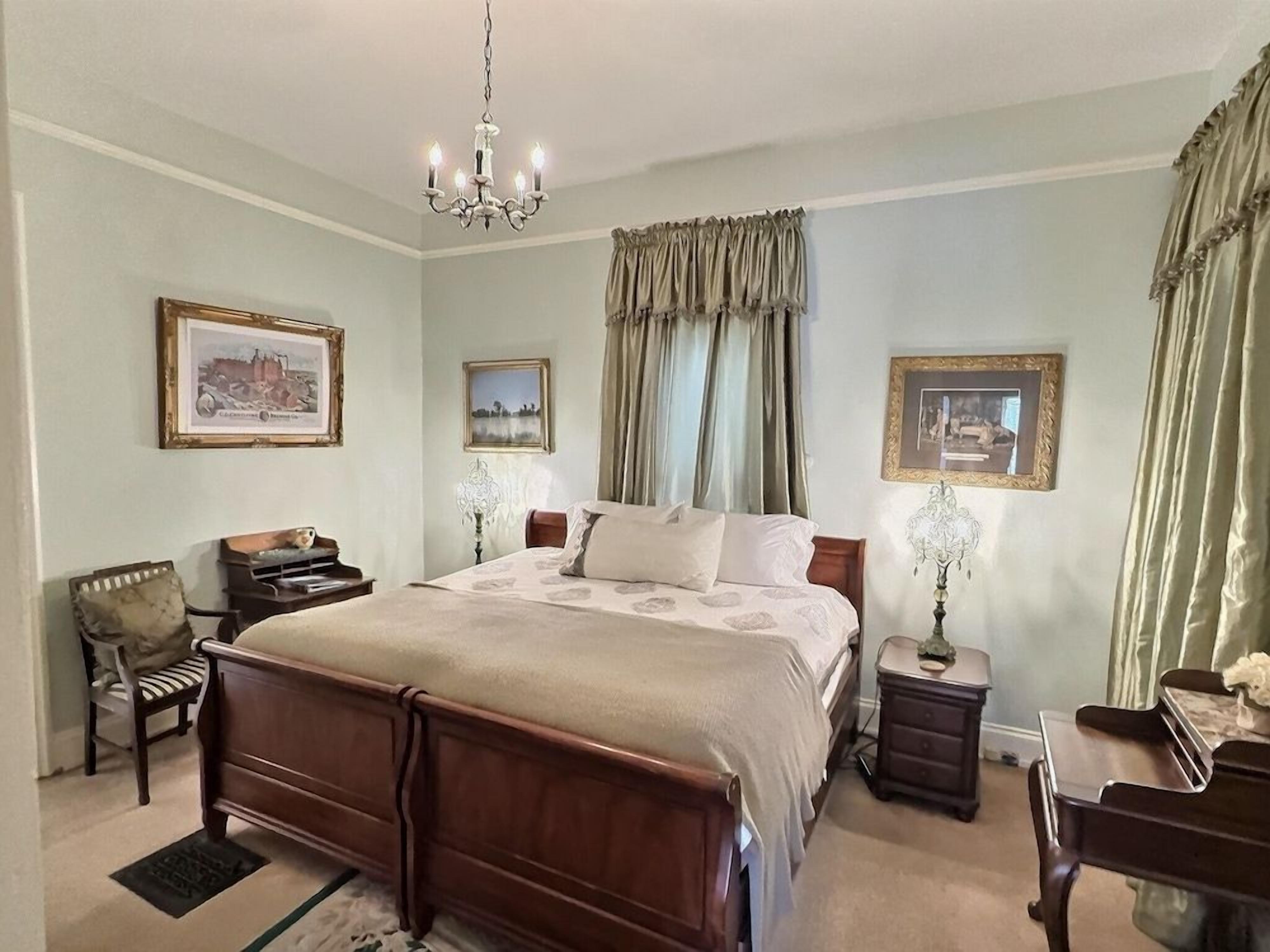 A bedroom with a large bed, bedside tables, a chair, and a piano.