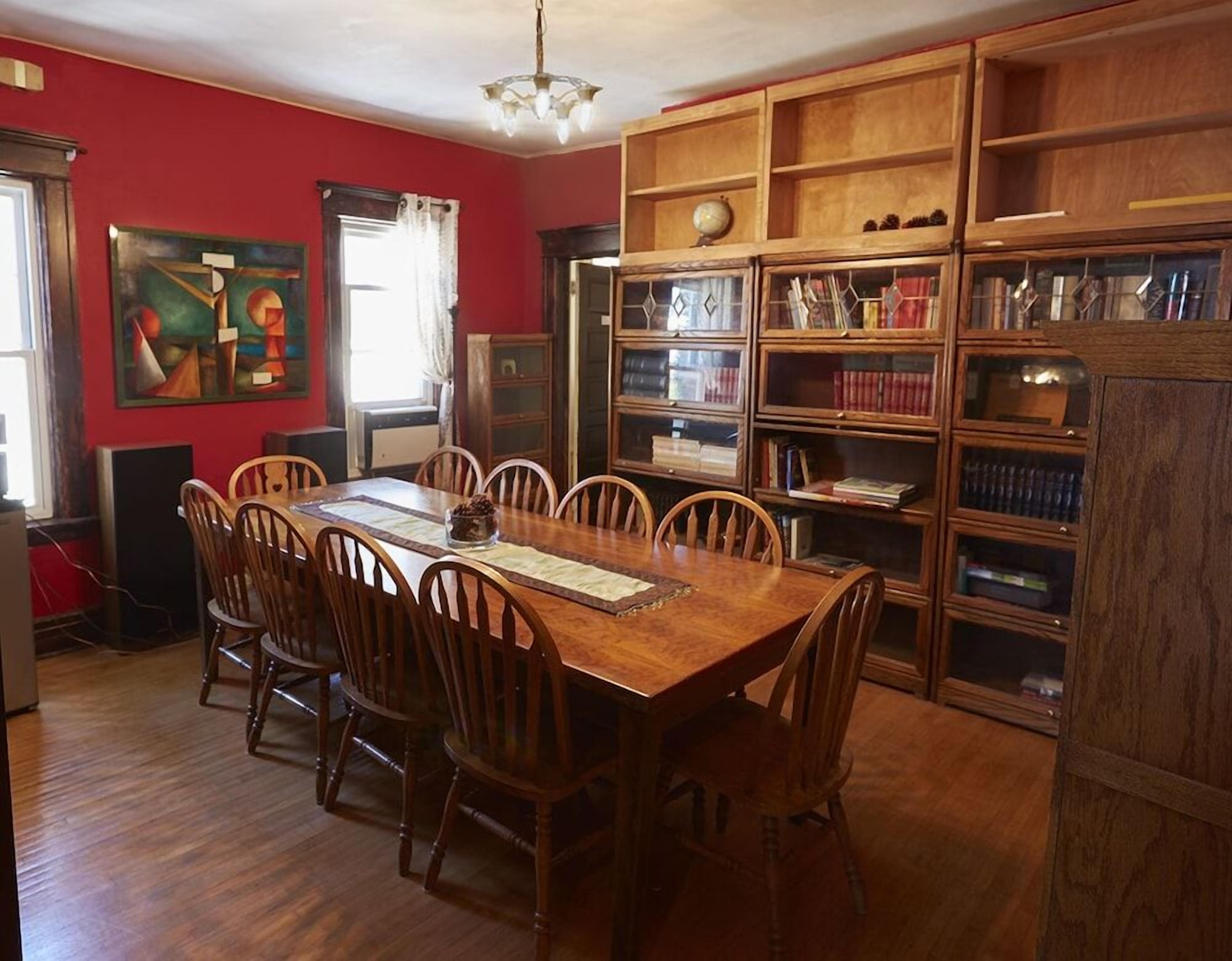 A dining room with a wooden table and chairs, a bookshelf with books, and a painting on the wall.