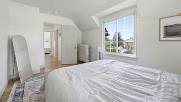 A bedroom with a large bed, a radiator, a window with a view, and a door leading to another room.
