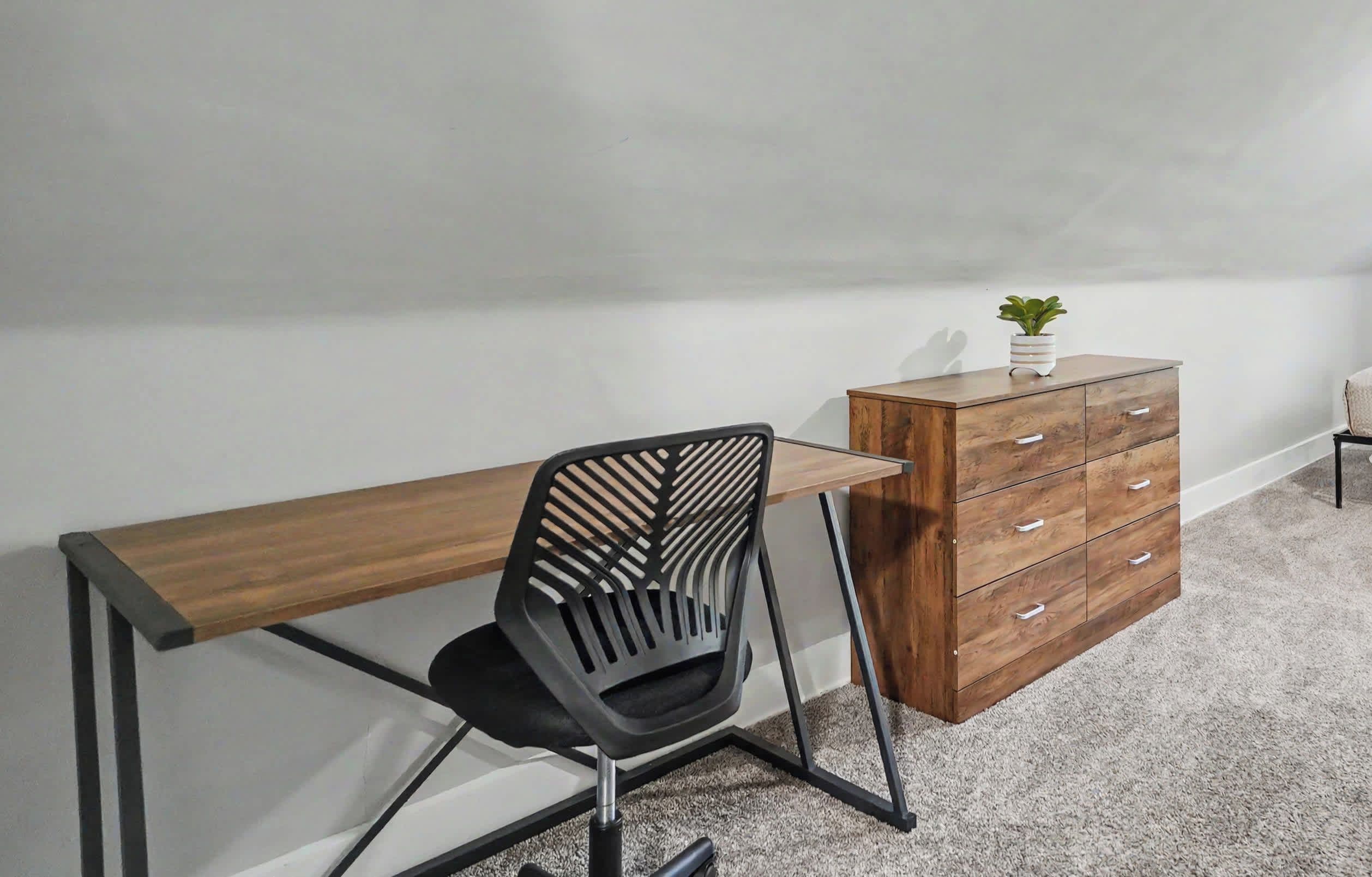 Una habitación con escritorio, silla, cómoda y una planta pequeña.