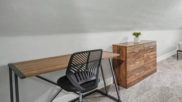 A room with a desk, a chair, a dresser, and a small plant.