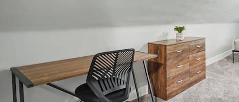 A room with a desk, a chair, a dresser, and a small plant.