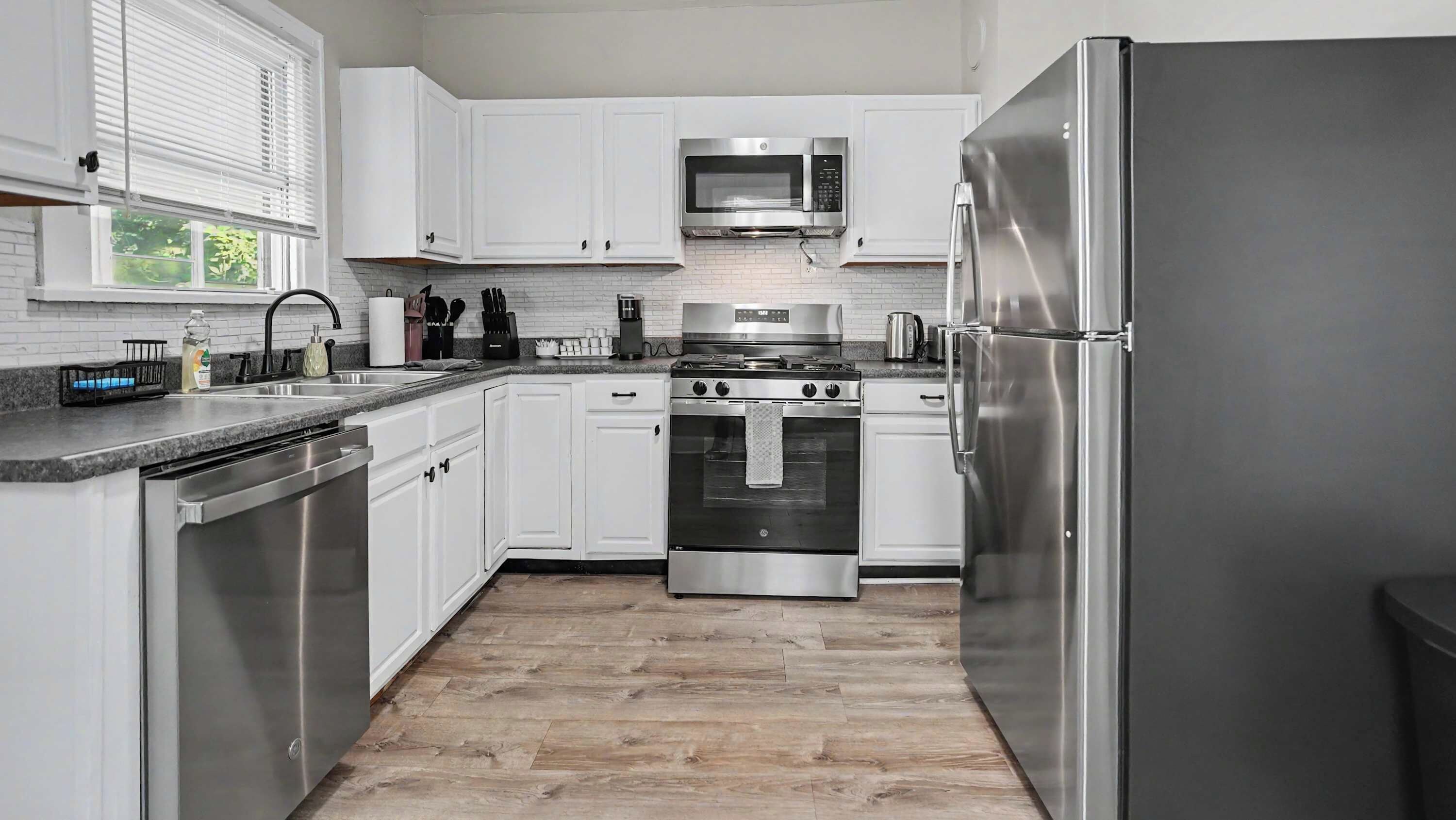 A modern kitchen with white cabinetry, stainless steel appliances, and a wood floor.