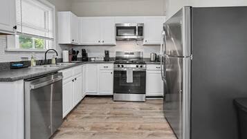 A modern kitchen with white cabinetry, stainless steel appliances, and a wood floor.