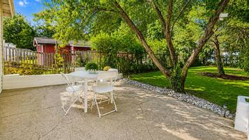 A patio with a table and chairs, surrounded by a garden and a wooden fence.