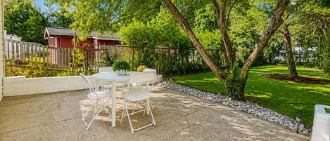 Un patio con mesa y sillas, rodeado de un jardín y una valla de madera.