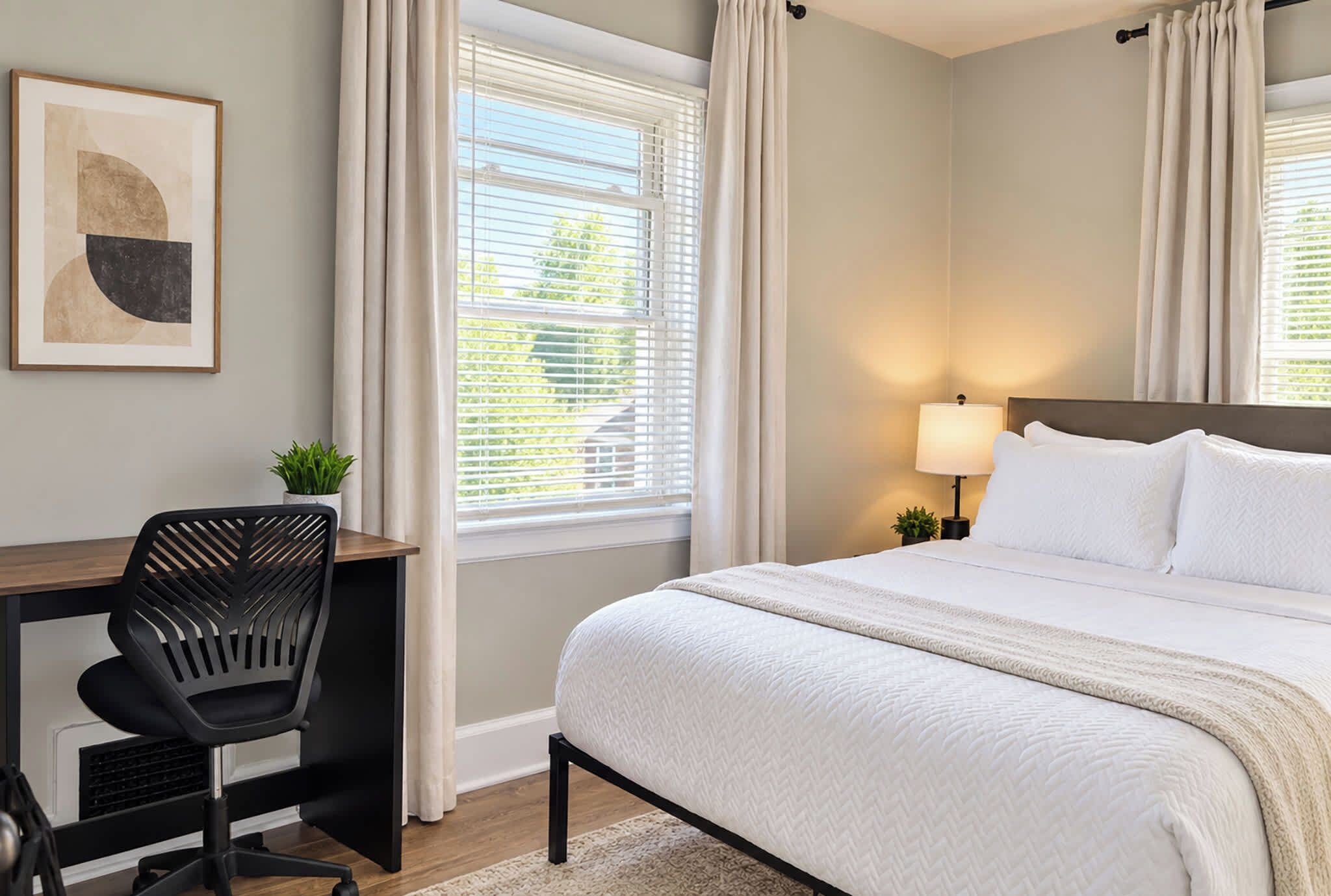A hotel room with a bed, a desk, a chair, a lamp, and a window with curtains.