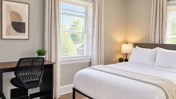A hotel room with a bed, a desk, a chair, a lamp, and a window with curtains.