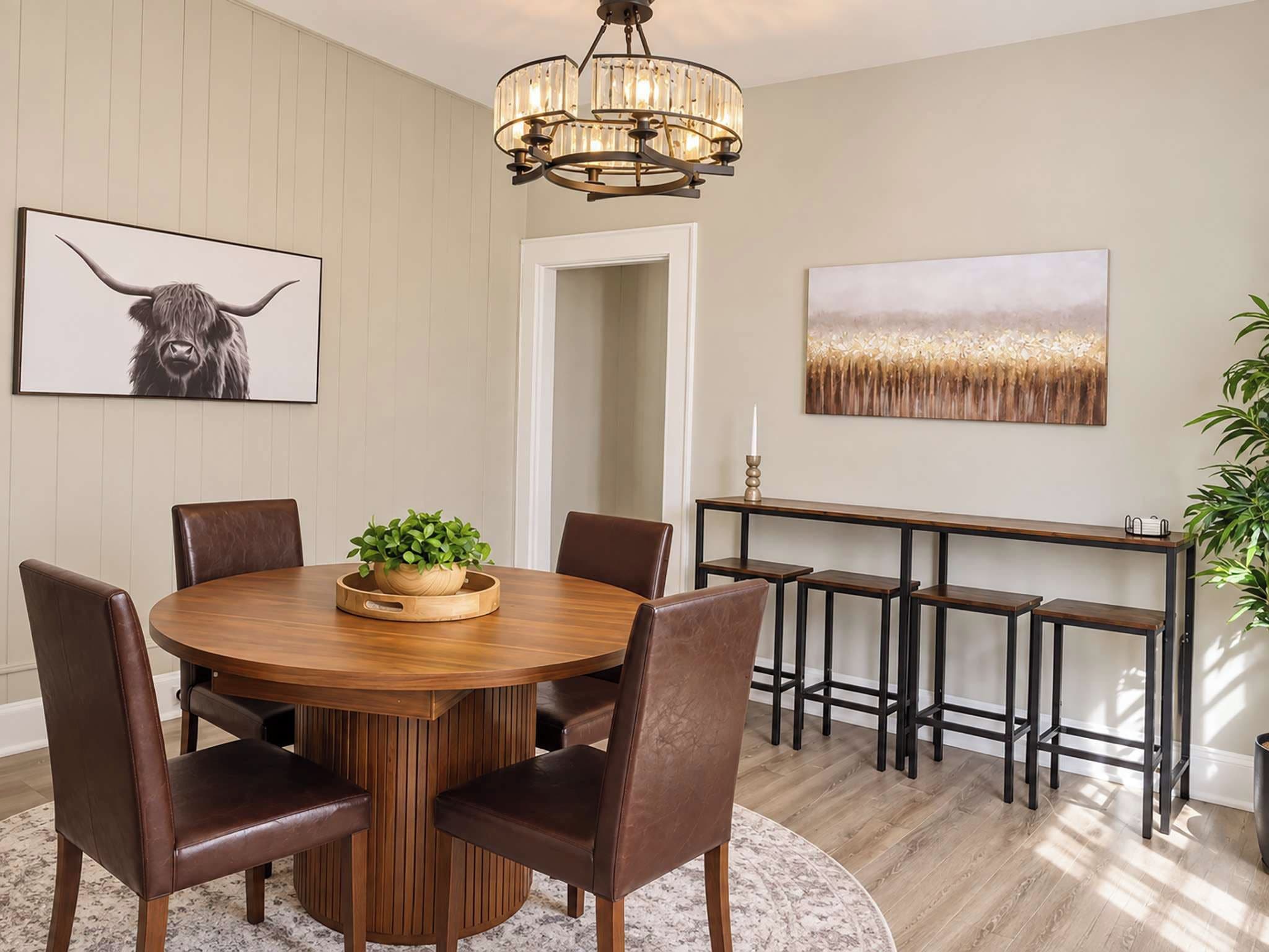 A dining area with a round wooden table, leather chairs, a chandelier, and artwork on the walls.