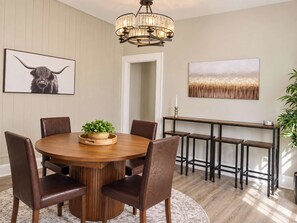 A dining area with a round wooden table, leather chairs, a chandelier, and artwork on the walls. - Cincy 5BR Retreat Xavier + Zoo Sleeps 7 (Cincinnati)