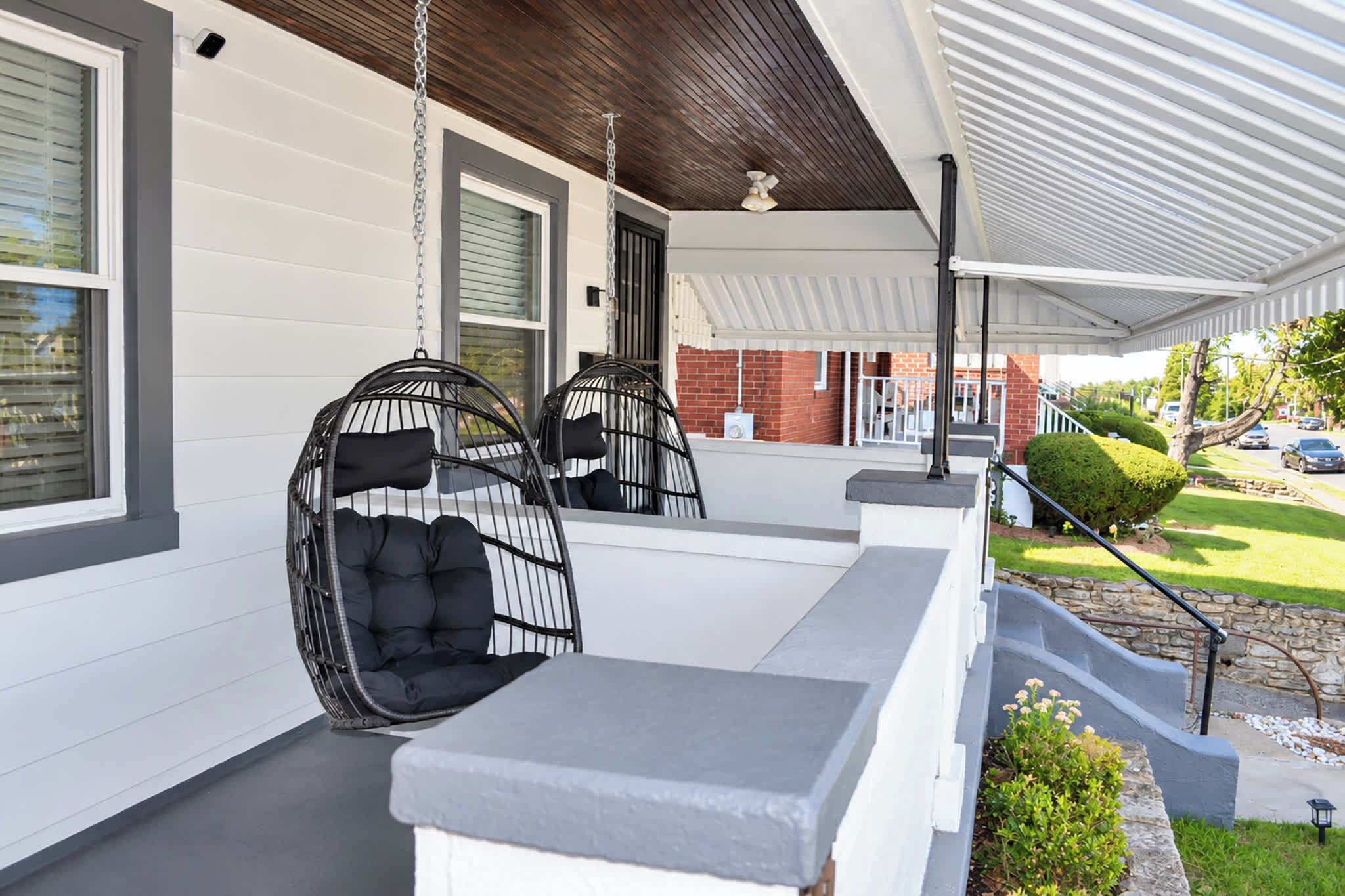 A covered porch with two black wicker chairs and a grey bench.