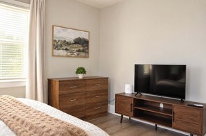 Ein Schlafzimmer mit einem Bett, einer Holzkommode, einem Fernseher und einem Bild an der Wand.