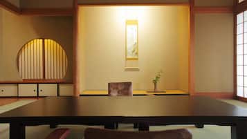 A traditional Japanese room with tatami flooring, a low table, a cushioned chair, a small table with a plant, and a sliding door with a decorative panel.