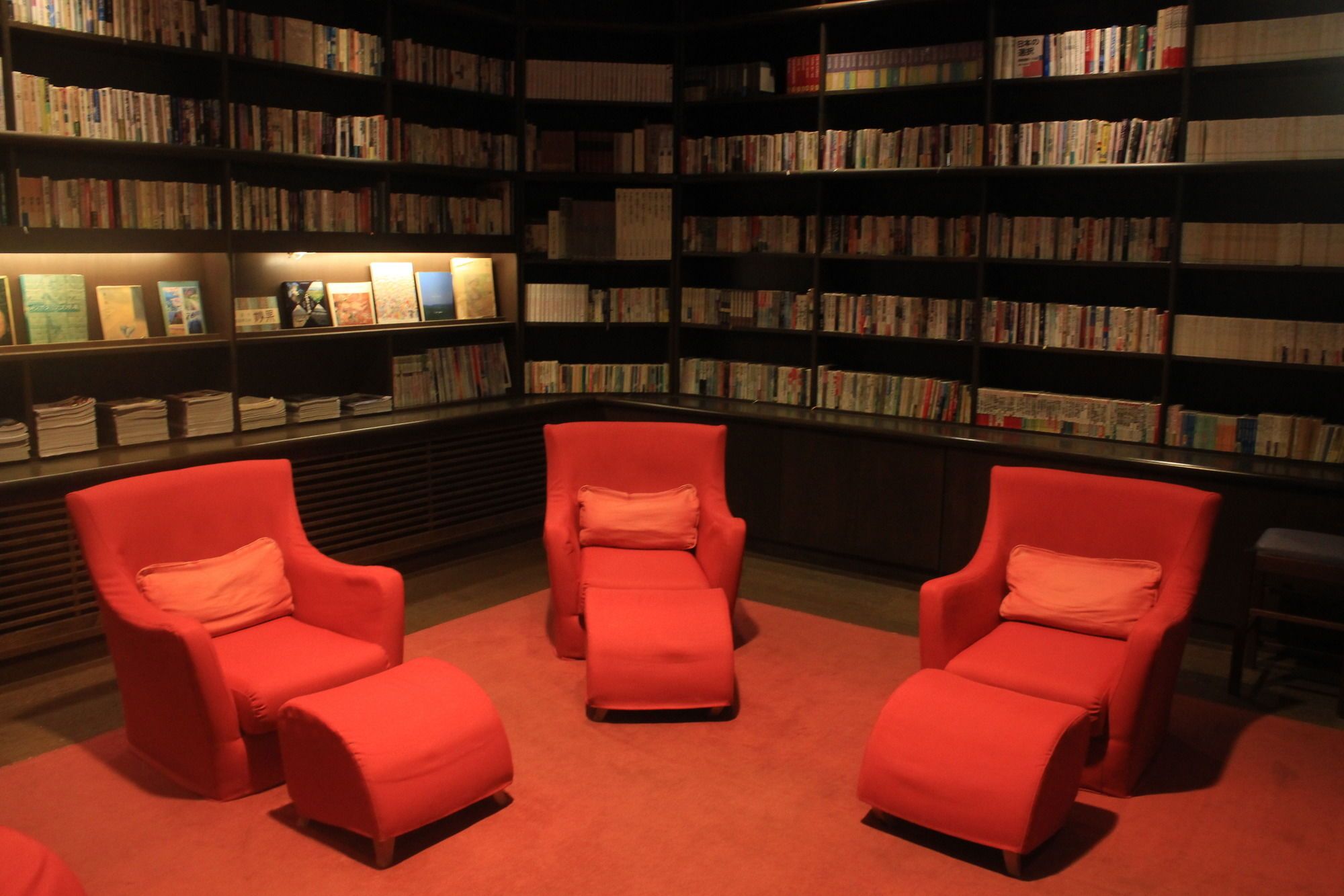 Una biblioteca con estanterías, tres sillones rojos y suelo alfombrado.