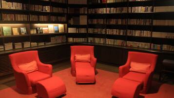 Una biblioteca con estanterías, tres sillones rojos y suelo alfombrado.