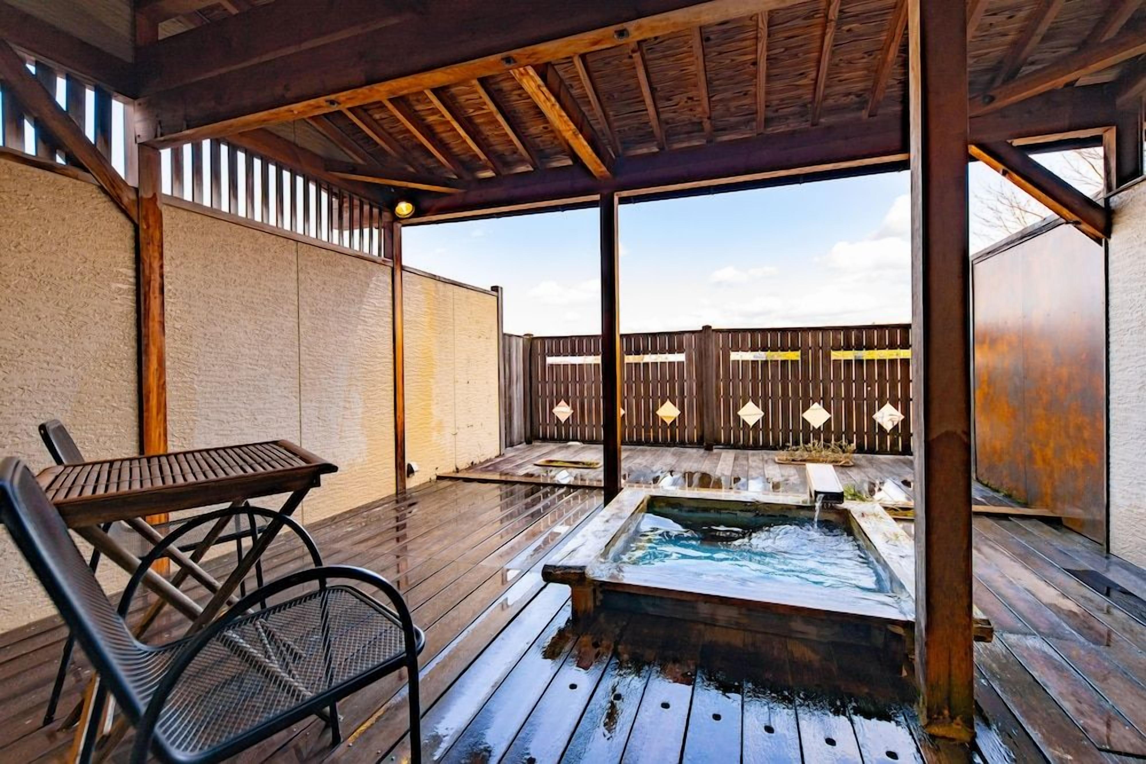 Un patio al aire libre con un jacuzzi, cubierta de madera, sillas de metal y una valla de madera.