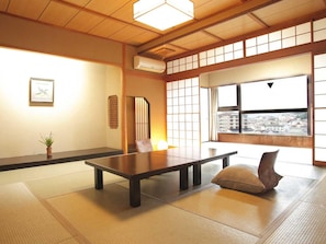 A traditional Japanese room with tatami flooring, a low table, and a view of a cityscape through large windows. - Yamashiro Onsen Onsen Meisoclub Fujiya (Kaga)