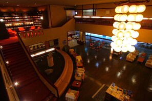 A multi-level hotel lobby with a central seating area, a staircase, and a bookshelf. - Yamashiro Onsen Onsen Meisoclub Fujiya (Kaga)