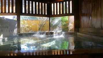 A hot spring bath with steam rising, surrounded by wooden walls and a view of trees.
