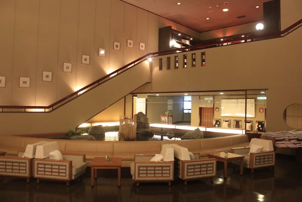 Vestíbulo de hotel con escalera, zona de estar y recepción.