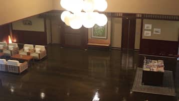 A spacious lobby with a central chandelier, seating area with sofas and tables, and a reception desk.