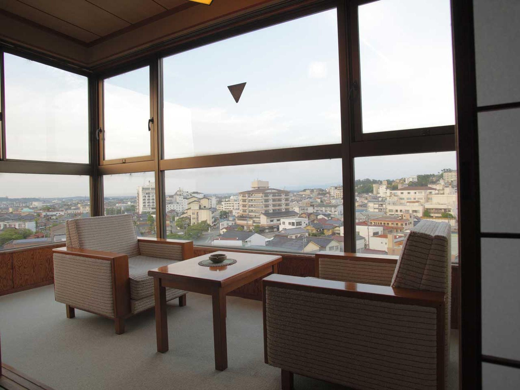 A room with a large window, a sofa, a table, and a view of a cityscape.