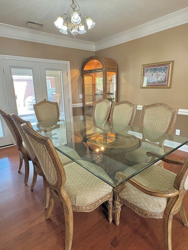 A dining area with a glass-top table surrounded by ornate chairs, a chandelier, and a framed picture on the wall.