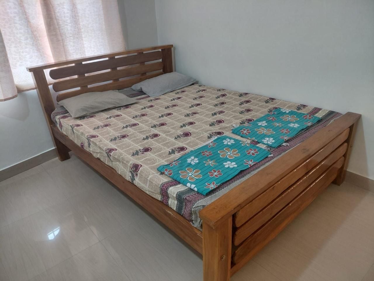 Una cama individual con estructura de madera, colcha estampada y manta floral color turquesa.