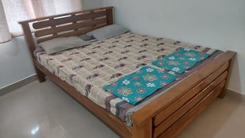 Una cama individual con estructura de madera, colcha estampada y manta floral color turquesa.