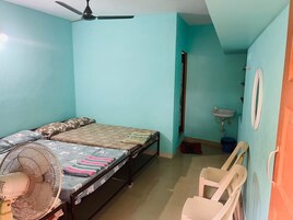 A room with a bed, a standing fan, a sink, and a mirror.