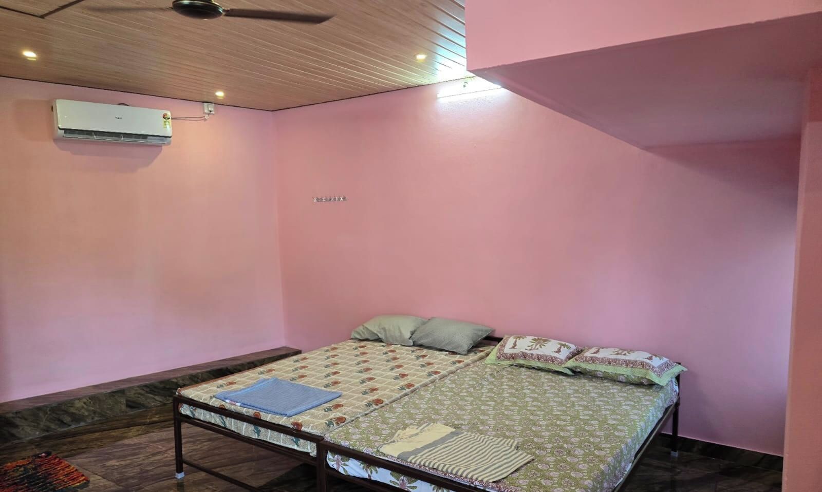 A bedroom with a bed, pillows, a blanket, a wooden ceiling, and an air conditioning unit.